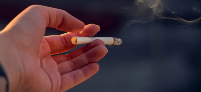 Mano sosteniendo un cigarrillo encendido con relación al cáncer de pulmón