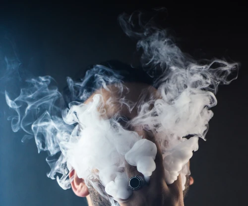 Hombre joven con humo de tabaco en la cara